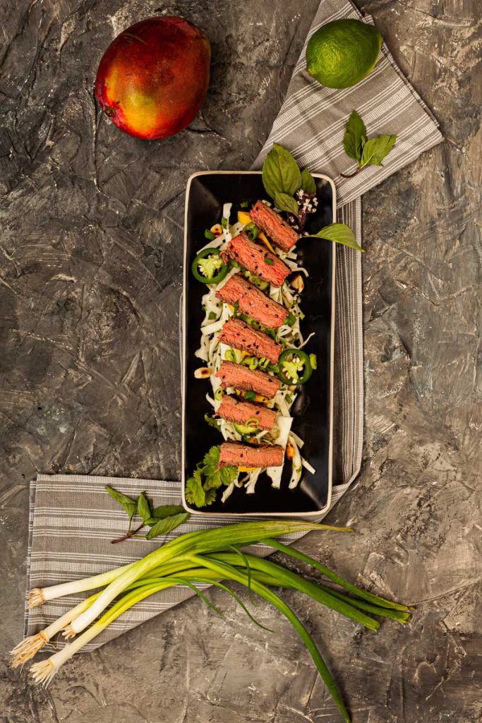 Flank steak with Asian mango, cucumber and cabbage salad on plates